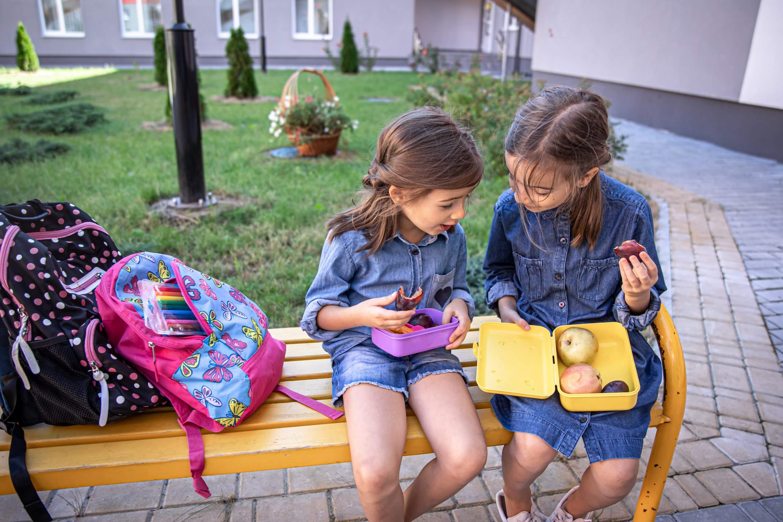 Back To School. Cute Little School Girls Sitting On Bench In Sch