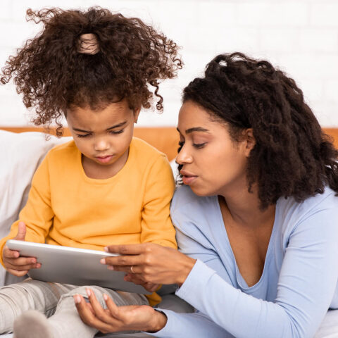 Black Mother Teaching Little Daughter To Use Digital Tablet Lyin