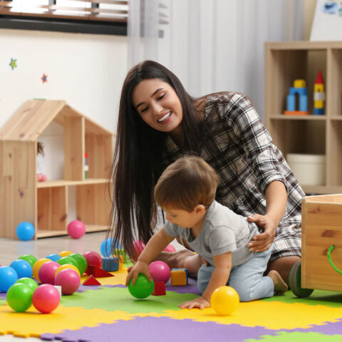 Young Nanny And Cute Little Baby Playing With Toys At Home